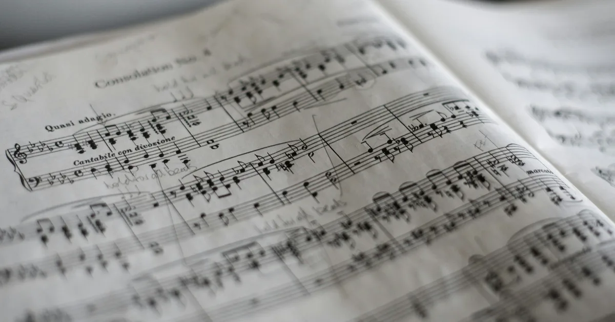 A close-up of old piano sheet music resting on a wooden upright piano.